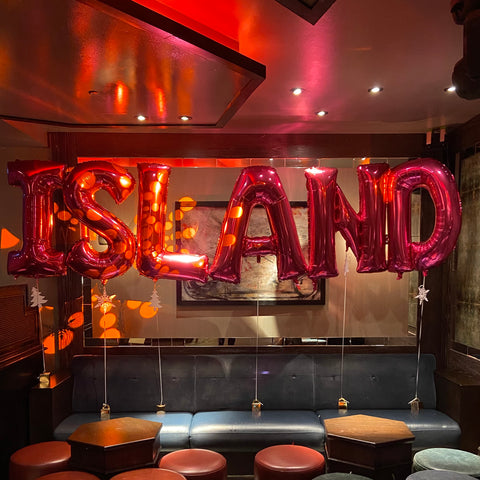 Giant hot pink foil helium letter balloons attached to weights and spelling out ISLAND